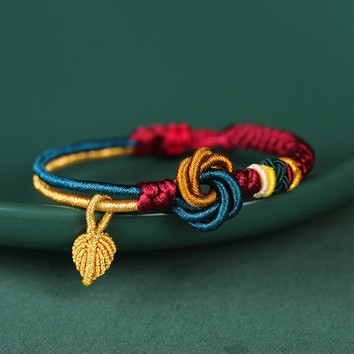 Tibetisches Armband mit bunten Knoten und goldenem Blatt-Anhänger auf grünem Hintergrund