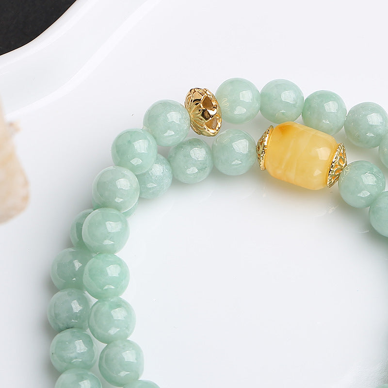 Jadegrünes Armband mit gelber Perle und goldenen Akzenten auf weißem Hintergrund.