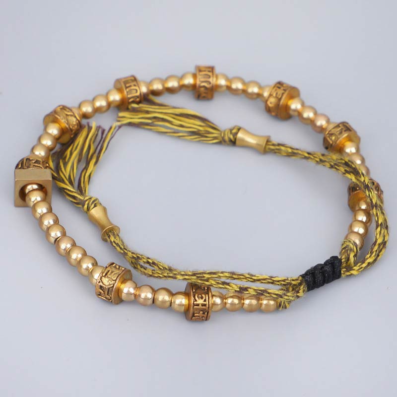 Tibetisches Armband mit goldenen Perlen und Quasten auf neutralem Hintergrund.