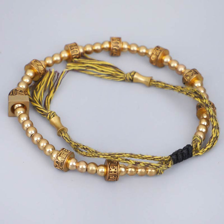 Tibetisches Armband mit goldenen Perlen und Quasten auf neutralem Hintergrund.
