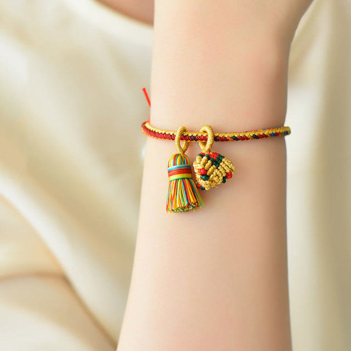 Buntes Armband mit goldenen Zongzi-Anhängern am Handgelenk getragen.