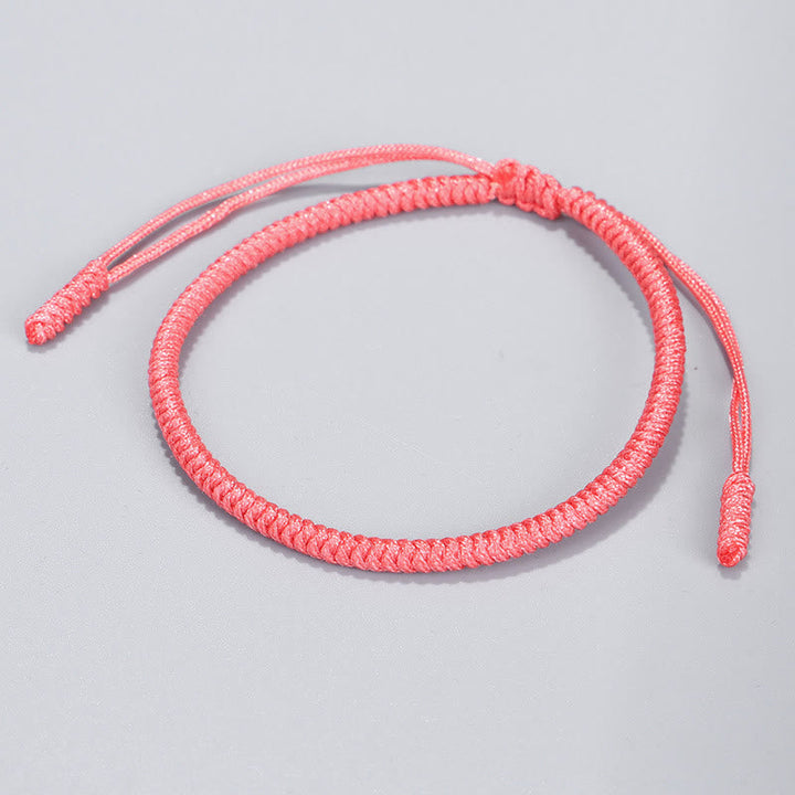 Tibetisches geflochtenes Armband in Korallenpink auf grauem Hintergrund.