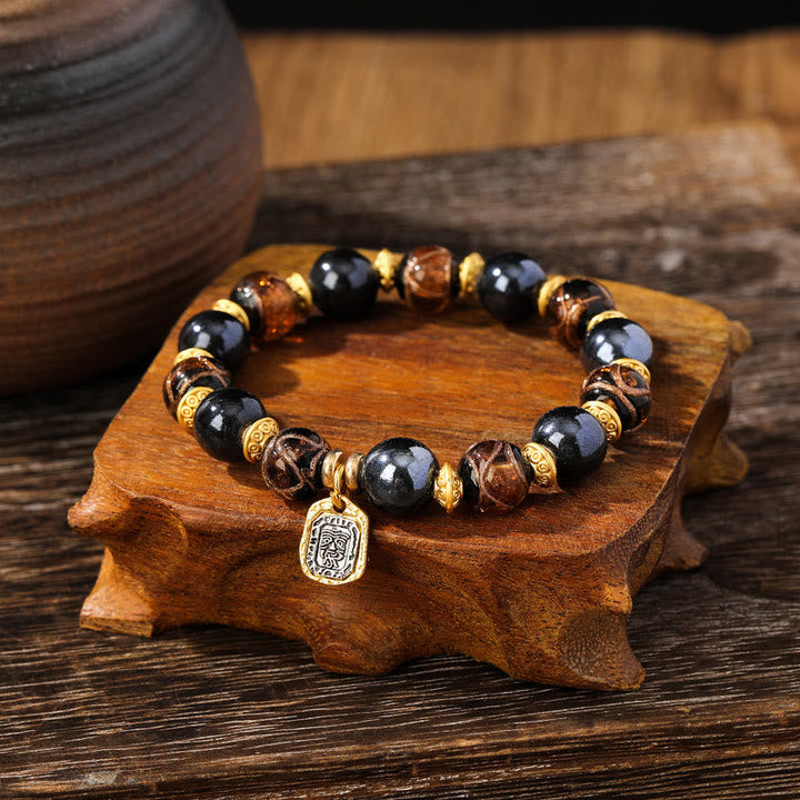 Armband Zakiram mit schwarzen Perlen und goldenen Akzenten auf Holz.