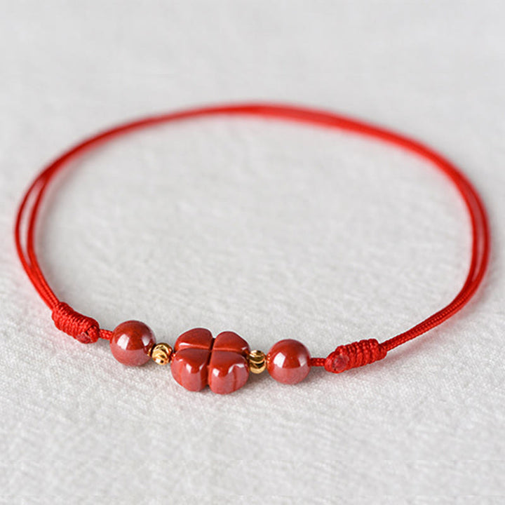 Rotes Armband Zinnober Kleeblatt mit goldenen Perlen auf weißem Hintergrund elastisch