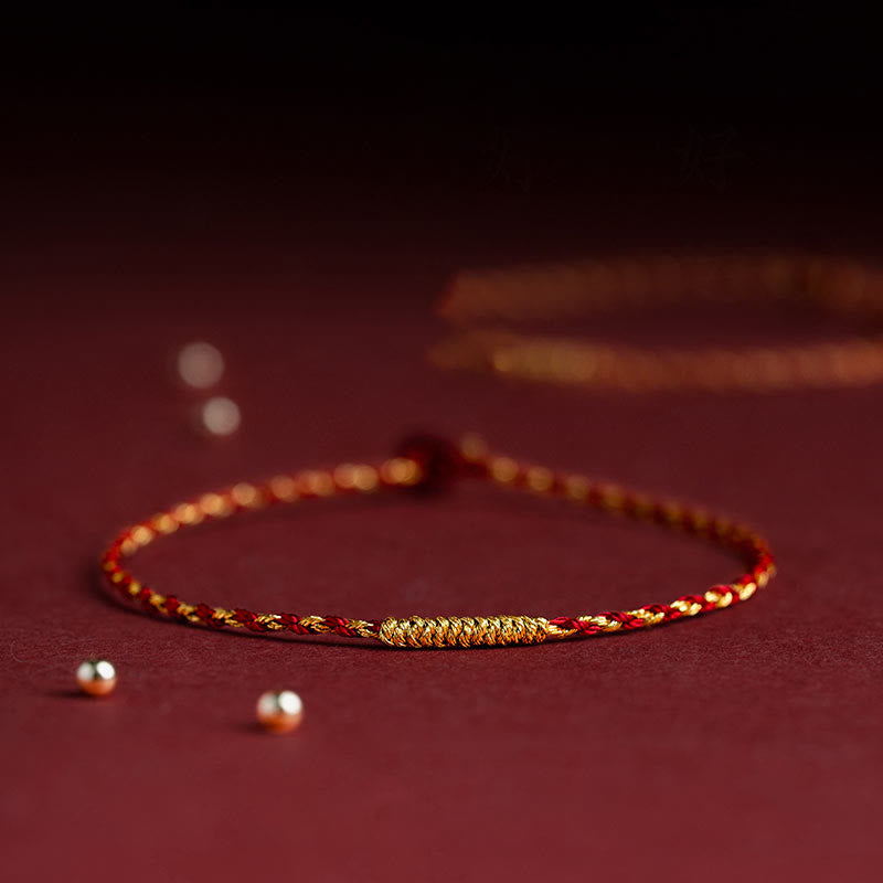 Geflochtenes goldenes Armband mit rotem Faden auf bordeauxrotem Hintergrund.
