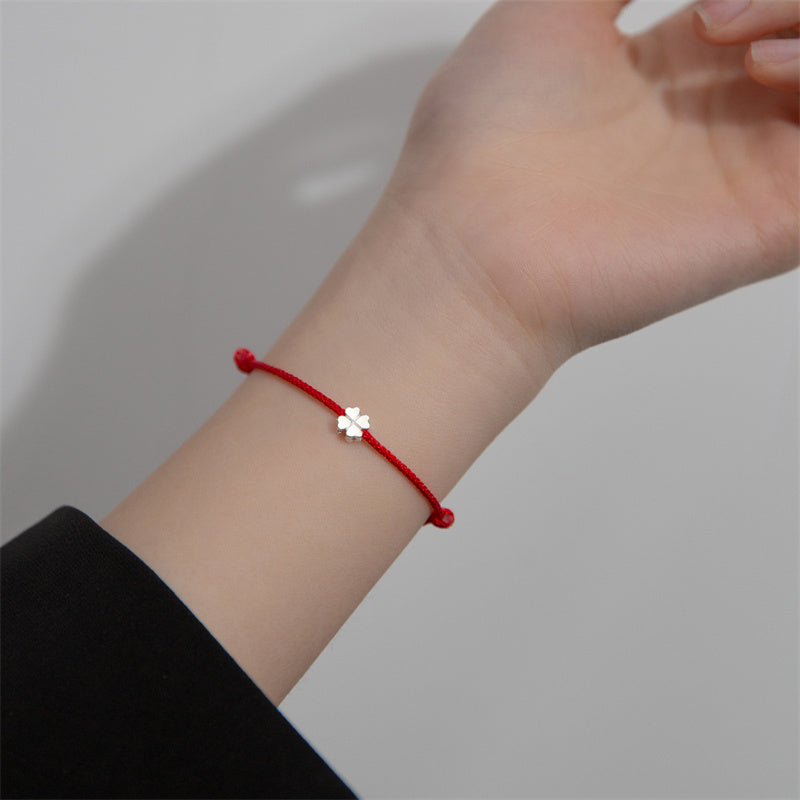 Rotes Armband mit silbernem Kleeblatt Charm am Handgelenk getragen.