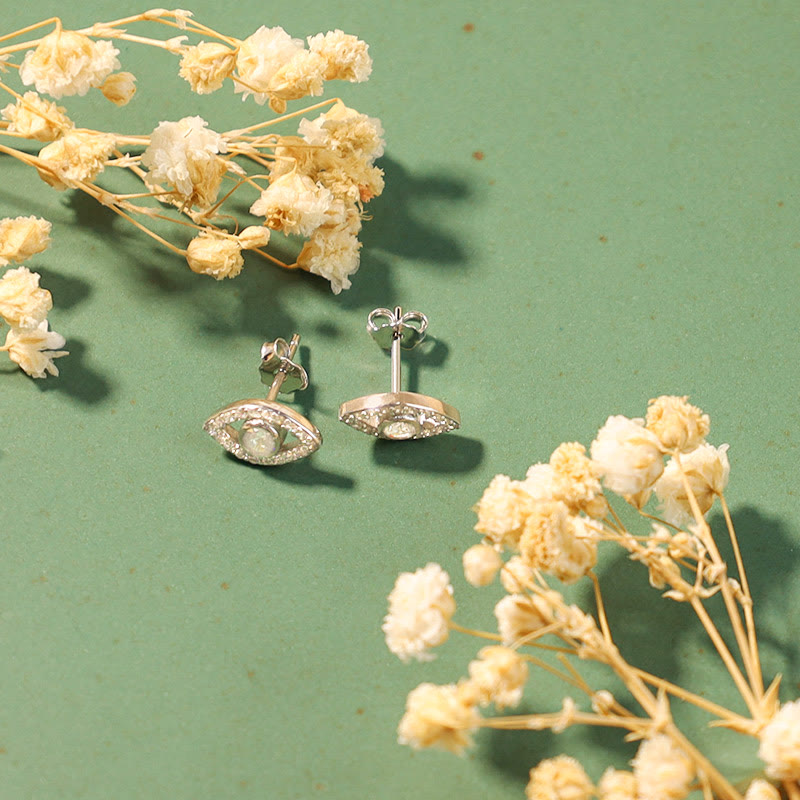 Silberne Ohrringe Böses Auge Design auf grünem Hintergrund Trockenblumen