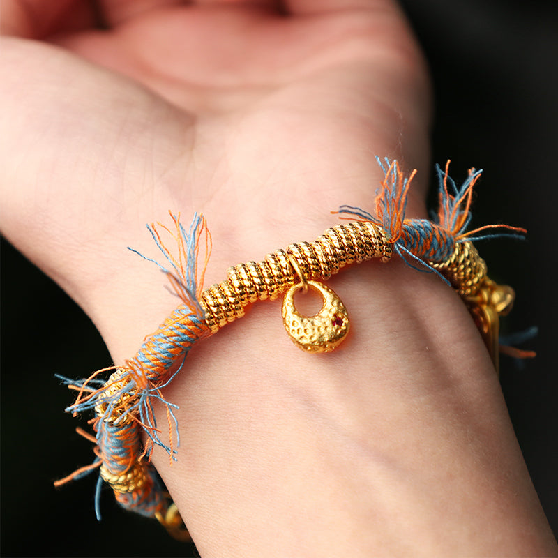 Tibetisches Armband mit goldenen Perlen und bunten Fasern am Handgelenk.