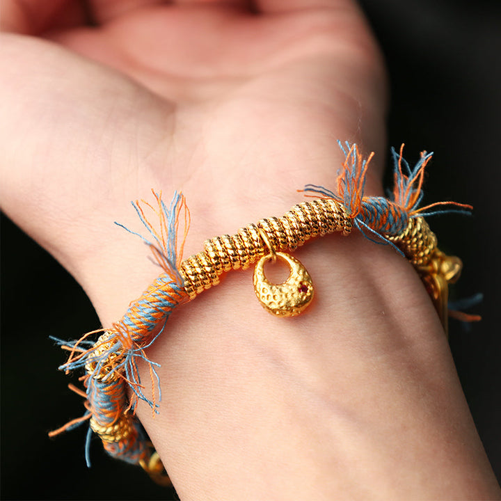 Tibetisches Armband mit goldenen Perlen und bunten Fasern am Handgelenk.