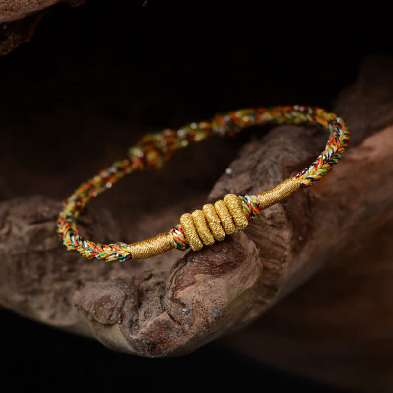 Buntes geflochtenes Armband mit goldenem Knoten auf Holz.