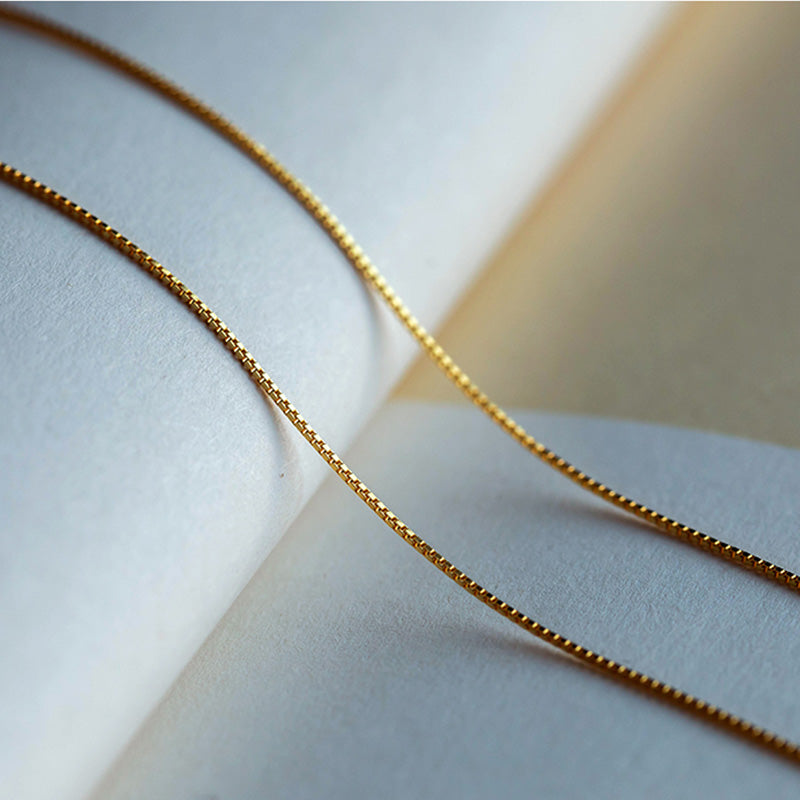 Goldene Halskette mit Box-Gliederkette auf hellem Hintergrund Schmuck.