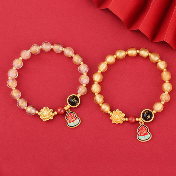 Zwei Armbänder mit roséfarbenen Perlen und goldenen Glücksbringern.