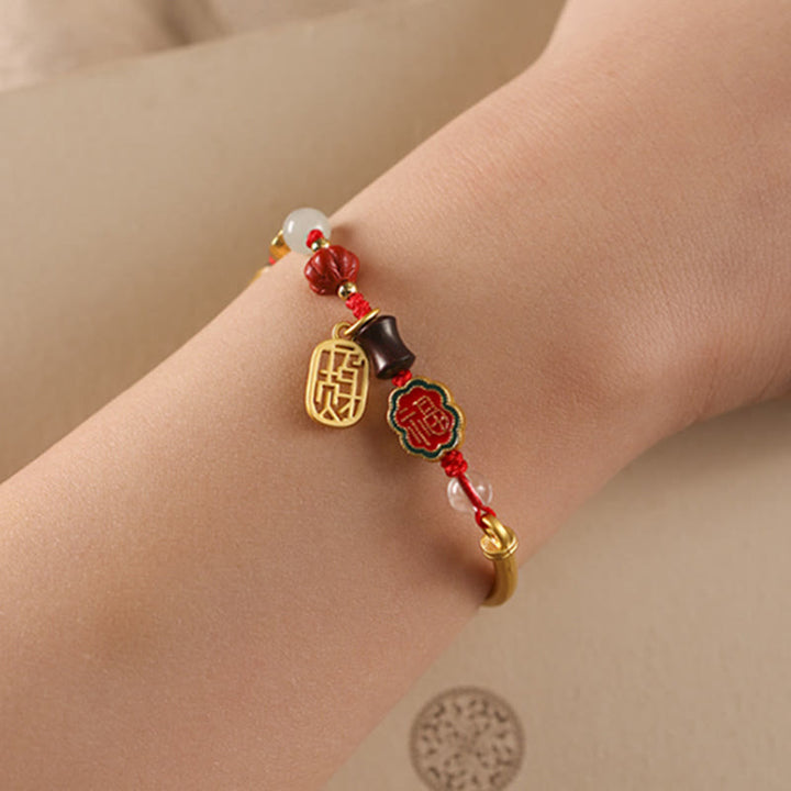 Armband Auspicious mit goldenen Anhängern und roten Perlen elegant.