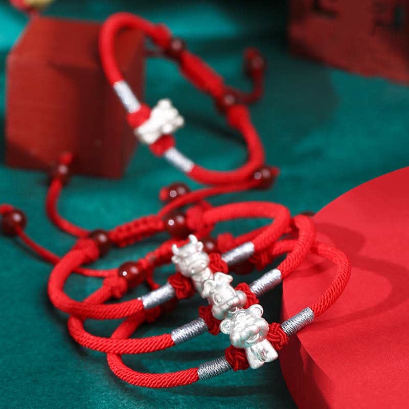 Rotes Armband 925 Silber Chinesisches Tierkreis mit silbernen Glücksbringer-Anhängern, Flat-Lay auf Türkis-Untergrund