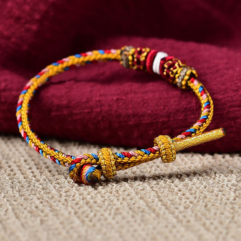 Geflochtenes rotes Schnur Karma Armband mit goldenen Elementen auf Textil, Detailaufnahme.