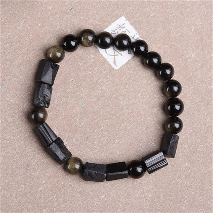 Obsidian Armband mit schwarzen Perlen und Hämatit-Elementen auf beigem Untergrund.