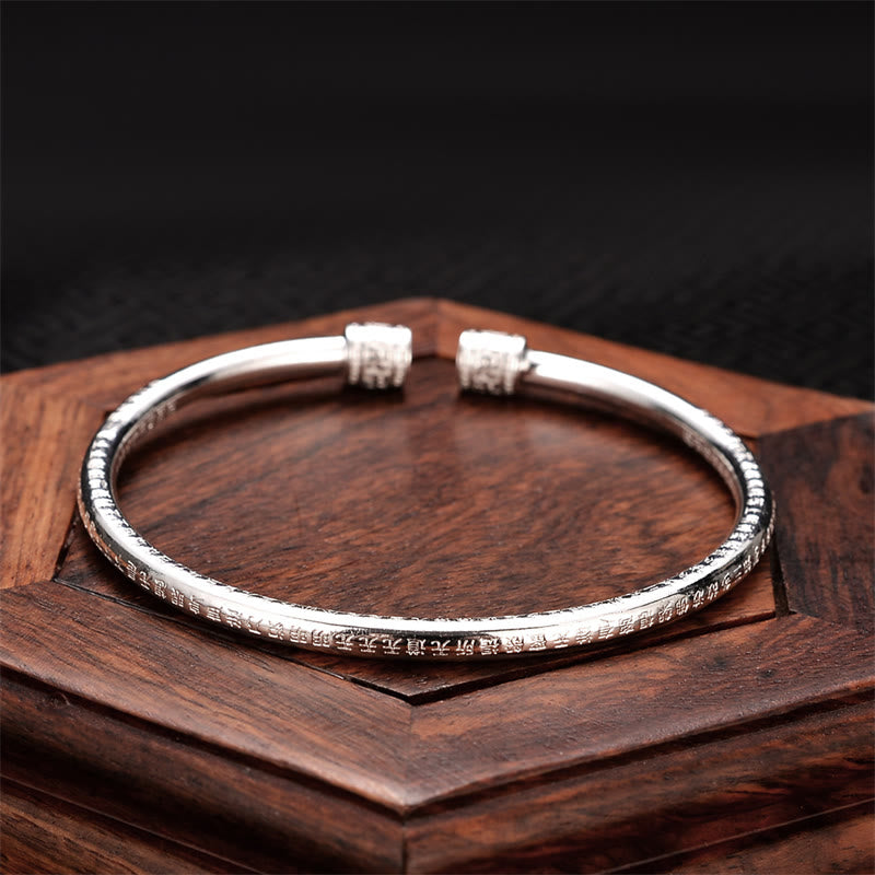 Silbernes Herzsutra Armband auf Holz, elegantes Design, strukturierte Oberfläche.