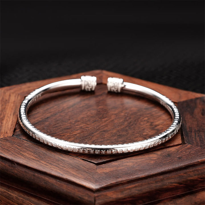 Silbernes Herzsutra Armband auf Holz, elegantes Design, strukturierte Oberfläche.