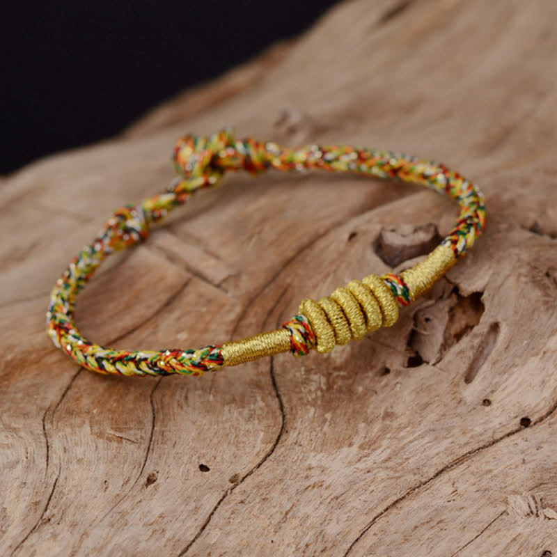 Bunt geflochtenes Armband mit goldenem Knoten auf Holz.
