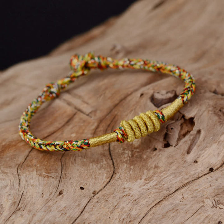 Bunt geflochtenes Armband mit goldenem Knoten auf Holz.