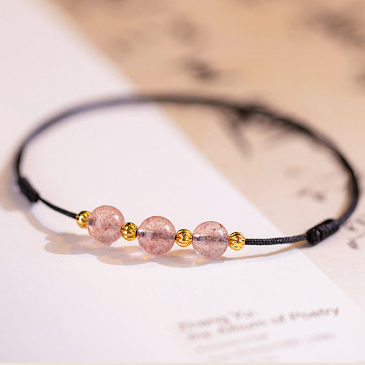 Armband Erdbeerquarz auf weißem Untergrund mit goldenen Perlen elegant präsentiert