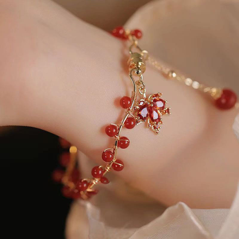 Rotes Armband mit Ahornblatt Charm und Glücksperlen am Handgelenk.