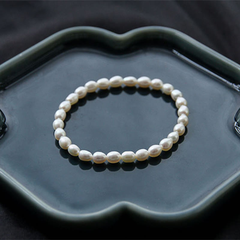Armband Perle – Heilung, elegantes Perlenarmband auf grauer Schale.