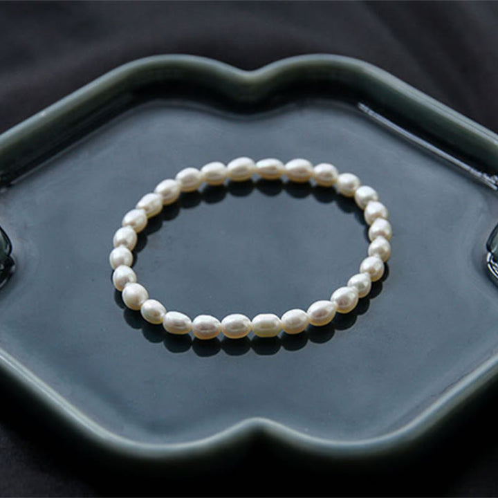 Armband Perle – Heilung, elegantes Perlenarmband auf grauer Schale.