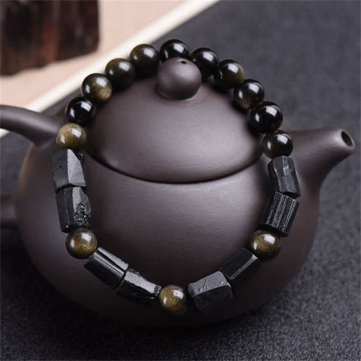Obsidian Armband mit goldenen Perlen auf grauem Teekanne Hintergrund, Naturstein Schmuck