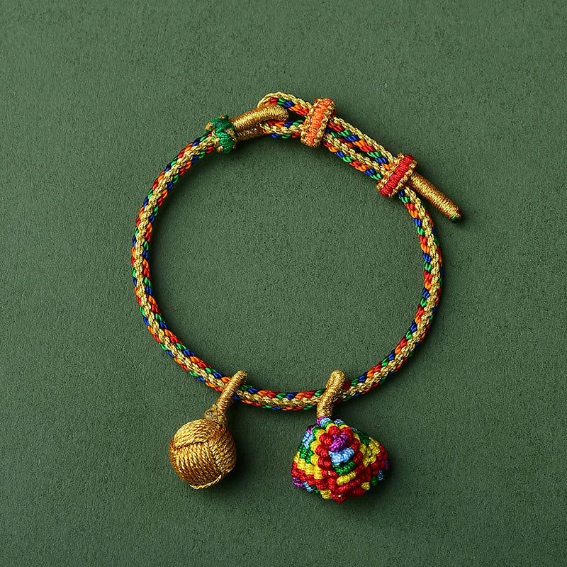 Buntes Armband mit goldenen Zongzi-Anhängern auf grünem Hintergrund.