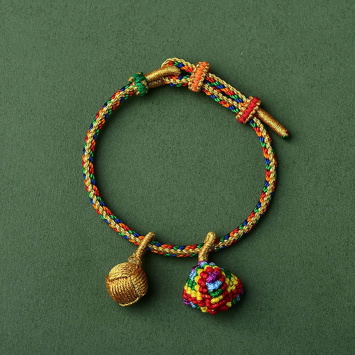 Buntes Armband mit goldenen Zongzi-Anhängern auf grünem Hintergrund.