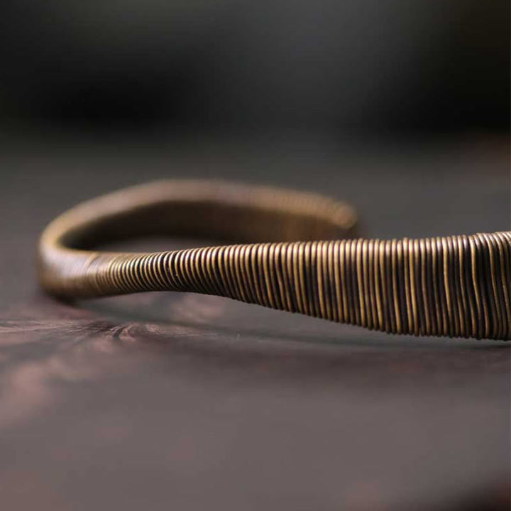 Kupfer Armband mit Spiralmuster liegt auf Holzoberfläche elegant gedreht.
