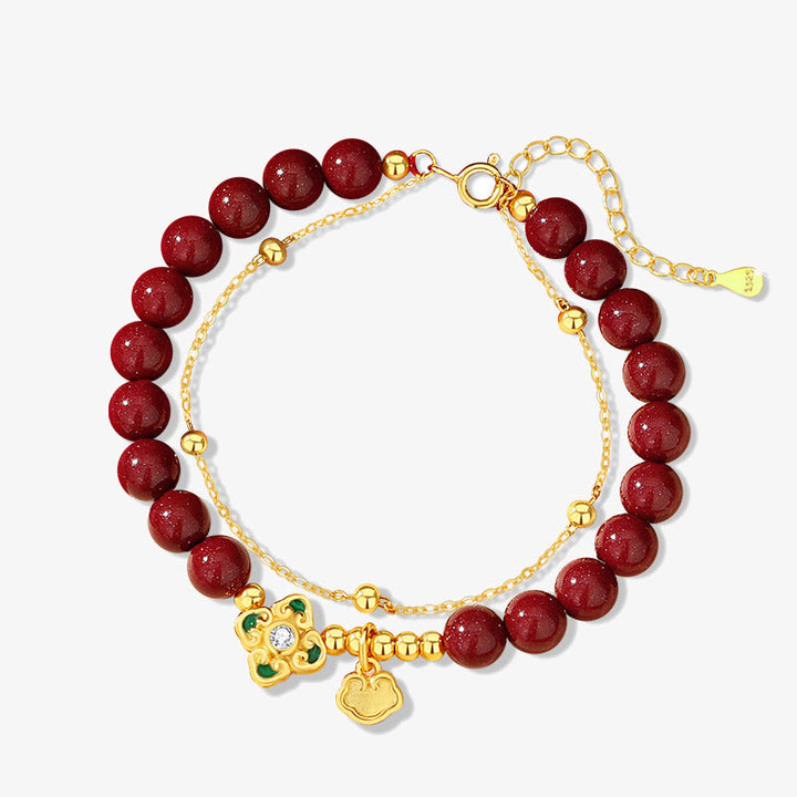 Armband mit roten Perlen, goldenem Kleeblatt und Anhänger auf weißem Hintergrund.