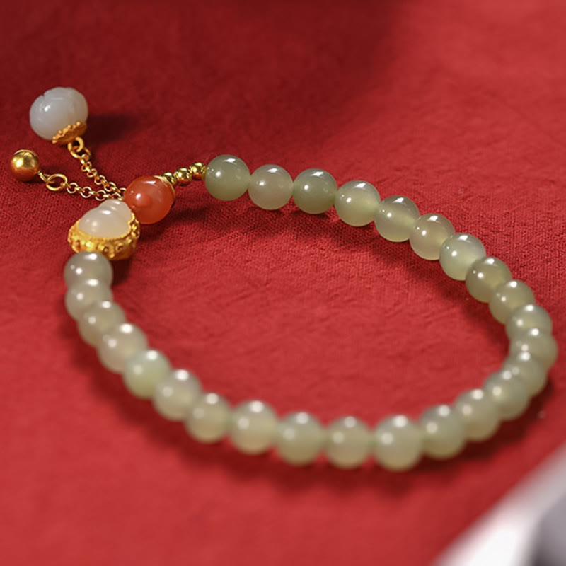Jade Armband mit goldenem Lotus-Anhänger auf rotem Hintergrund elegant.