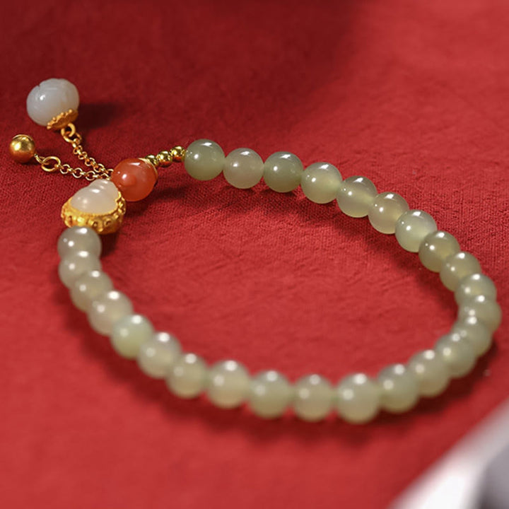 Jade Armband mit goldenem Lotus-Anhänger auf rotem Hintergrund elegant.