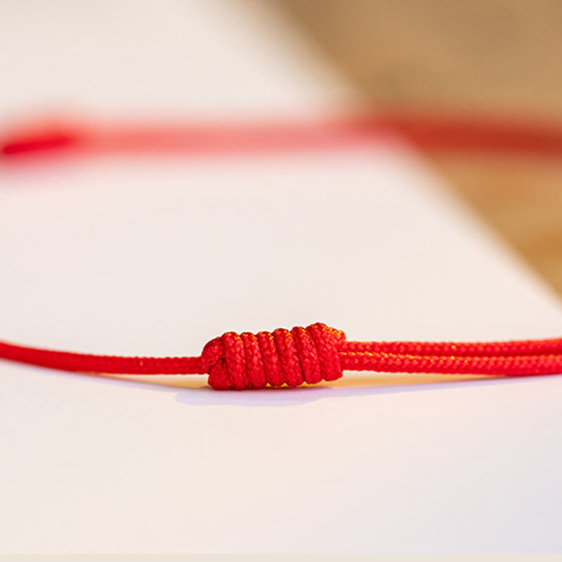 Rotes Armband Zinnober Kleeblatt mit Knoten auf weißem Untergrund Nahaufnahme