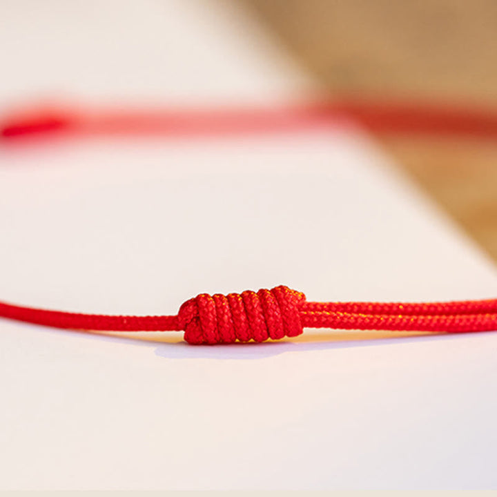 Rotes Armband Zinnober Kleeblatt mit Knoten auf weißem Untergrund Nahaufnahme