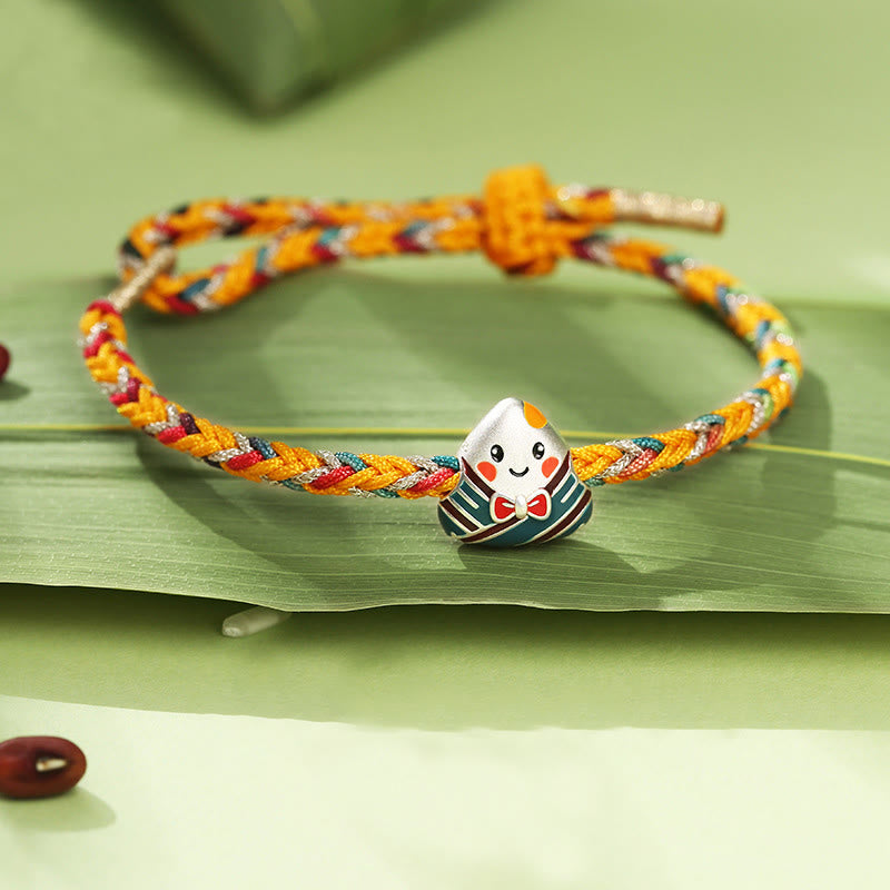 Buntes Seil-Armband mit silbernem Drachen-Charm auf Blatt.