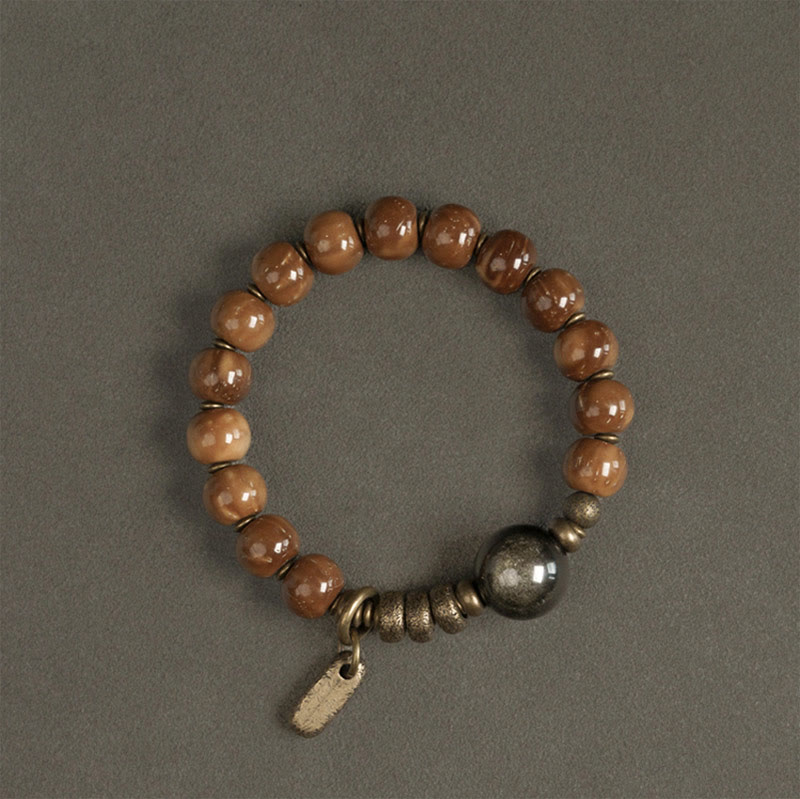 Armband mit braunen Holzperlen und Metallakzenten auf grauem Hintergrund.