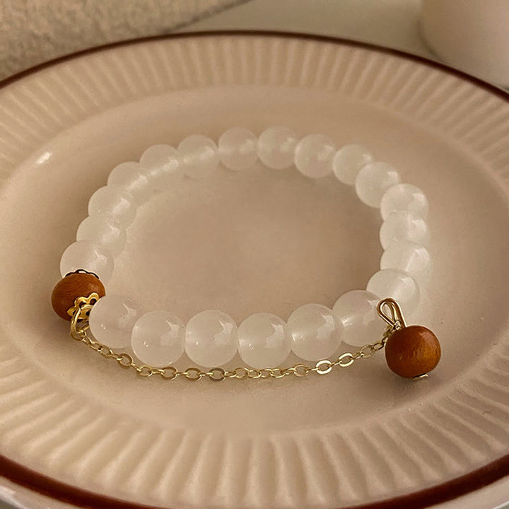 Weißes Perlenarmband mit Sandelholz-Perlen auf Porzellanteller.