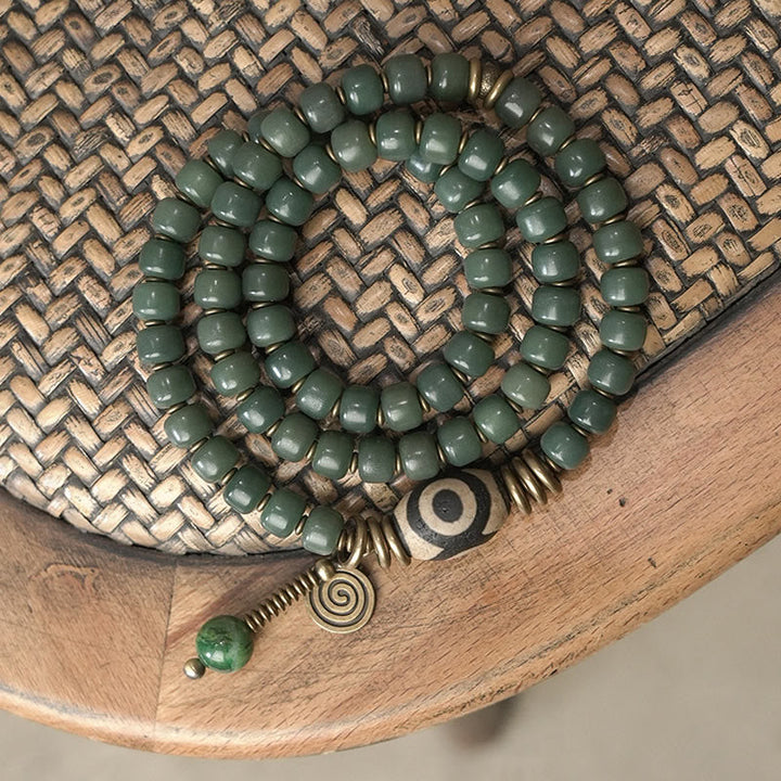 Grünes Bodhi Armband mit Spiralanhänger auf Holzuntergrund.