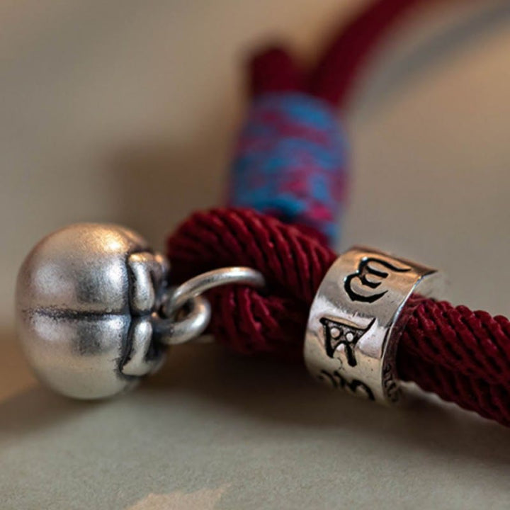 Armband 925 Silber Om Mani Padme Hum am Handgelenk mit roter Schnur getragen.