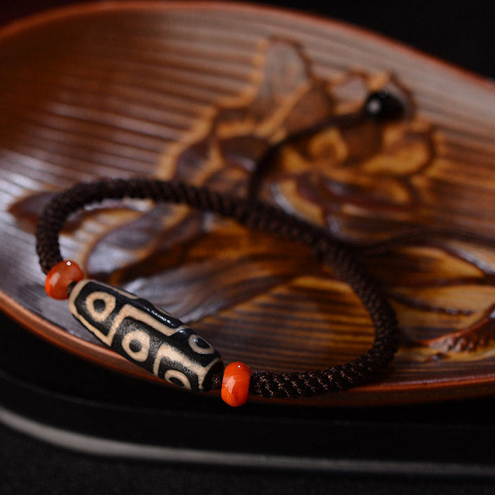 Dzi-Perle Neun Augen Armband mit roten Korallenkugeln auf Holzschale Nahaufnahme