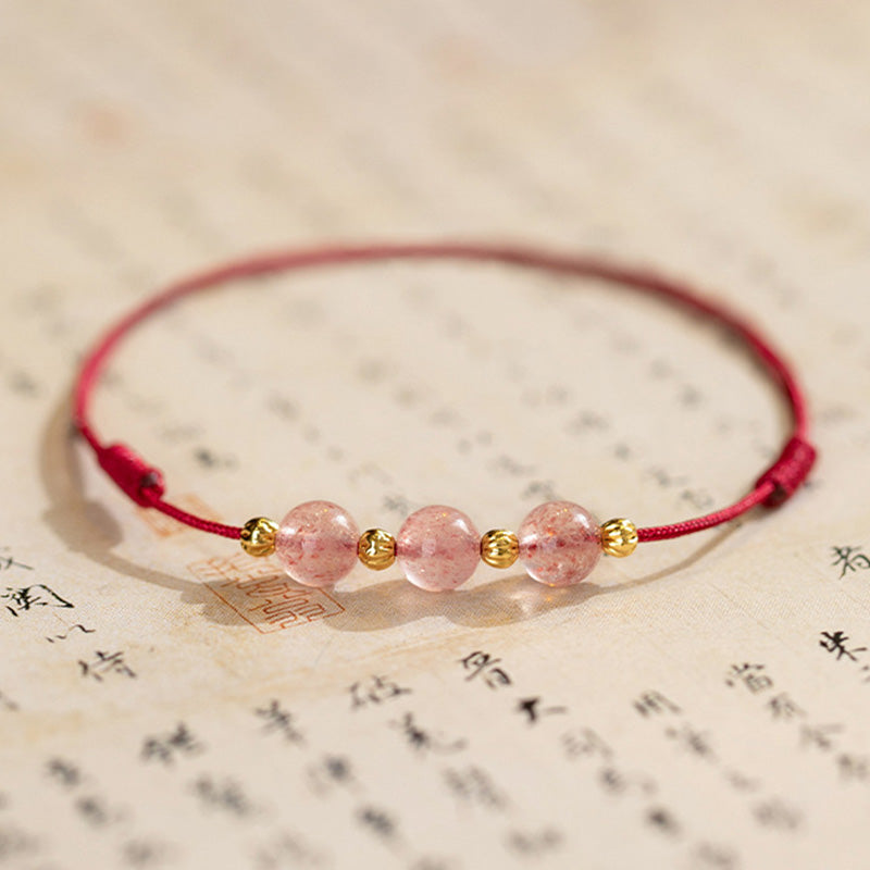 Armband Erdbeerquarz mit rosa Steinen und goldfarbenen Perlen auf bedrucktem Hintergrund.