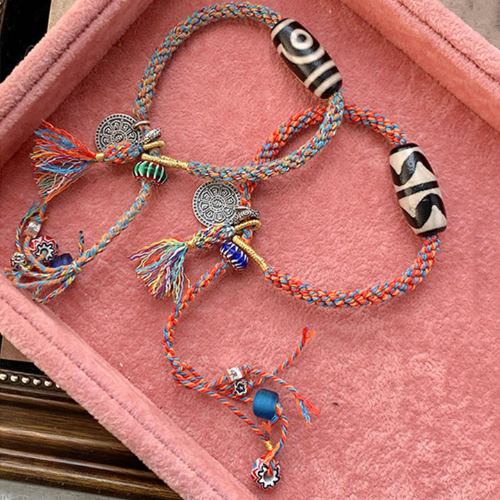 Bunte Armbänder mit Silberperlen und Quasten auf rosa Stoff.