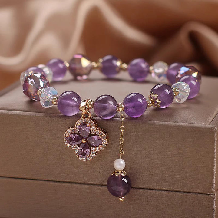 Amethyst Kristall Armband mit Kleeblatt Anhänger auf beiger Oberfläche.