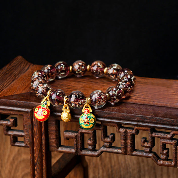 Dunkelrotes Armband mit goldenen Anhängern auf Holzoberfläche.