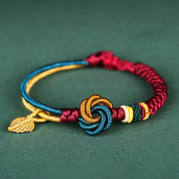 Tibetisches Armband mit bunten Knoten und goldenem Blatt auf grünem Hintergrund.