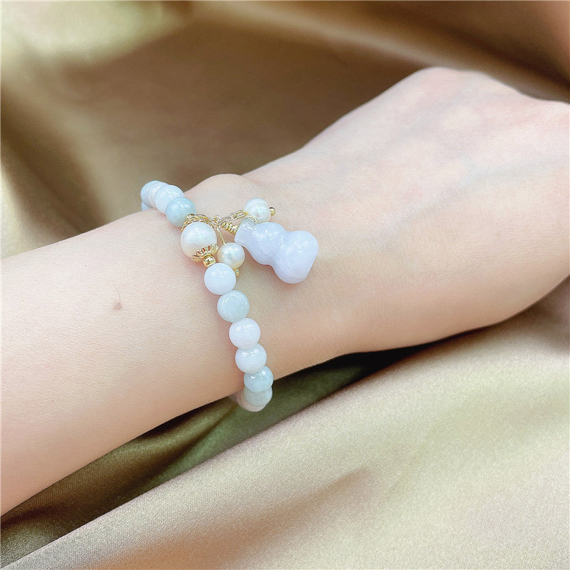 Jade Armband am Handgelenk mit weißen Perlen und goldenem Charm getragen.
