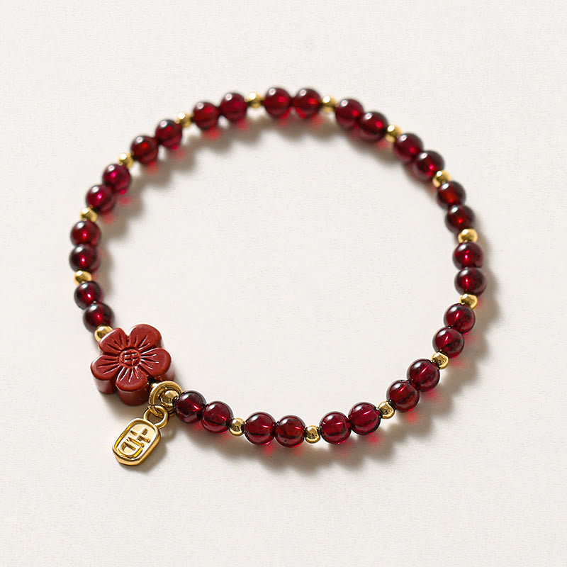 Rotes Granat Armband mit Blume und Gold Charm auf weißem Hintergrund.